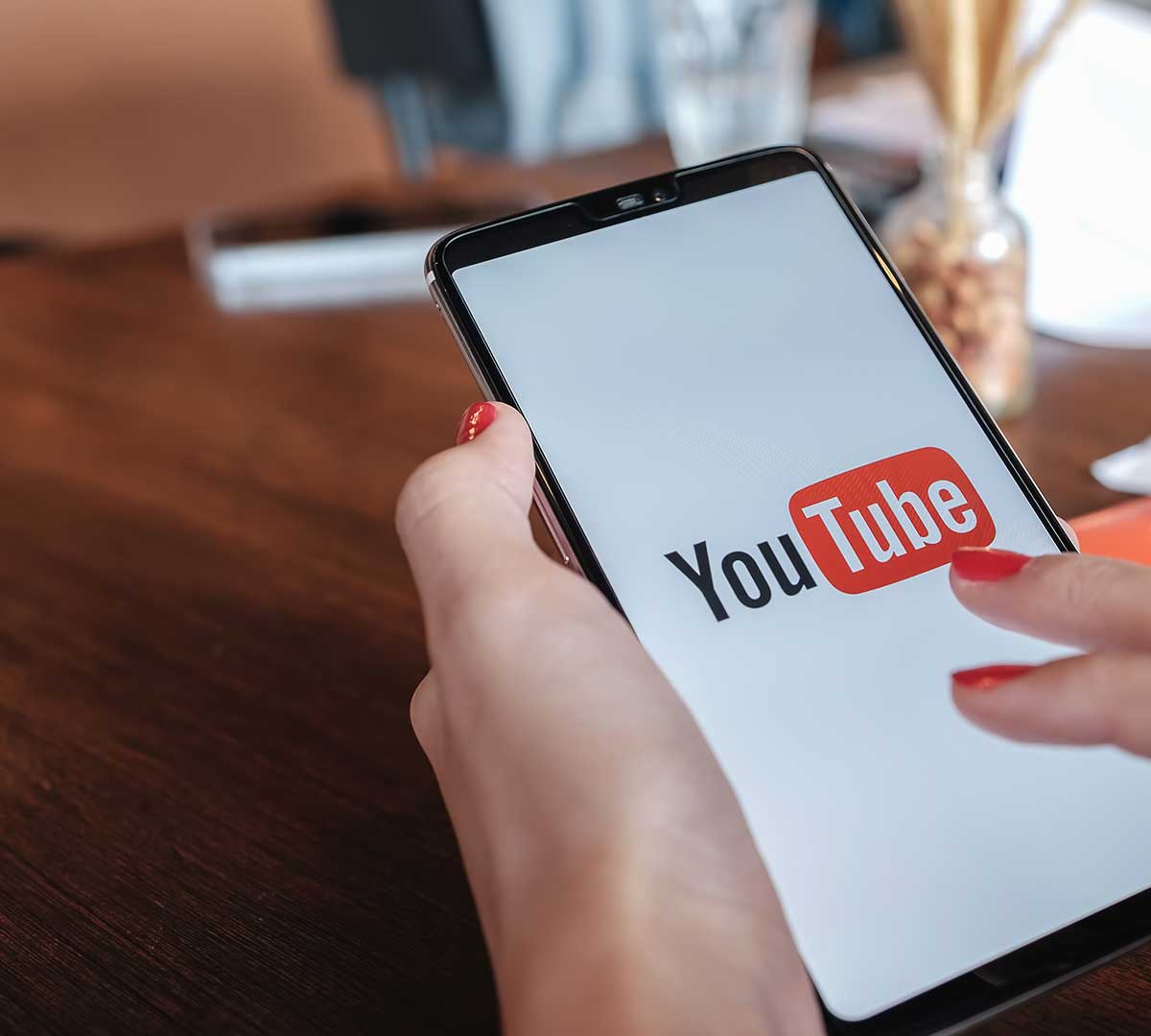 A cellphone is being held, the smartphone screen shows the YouTube logo.